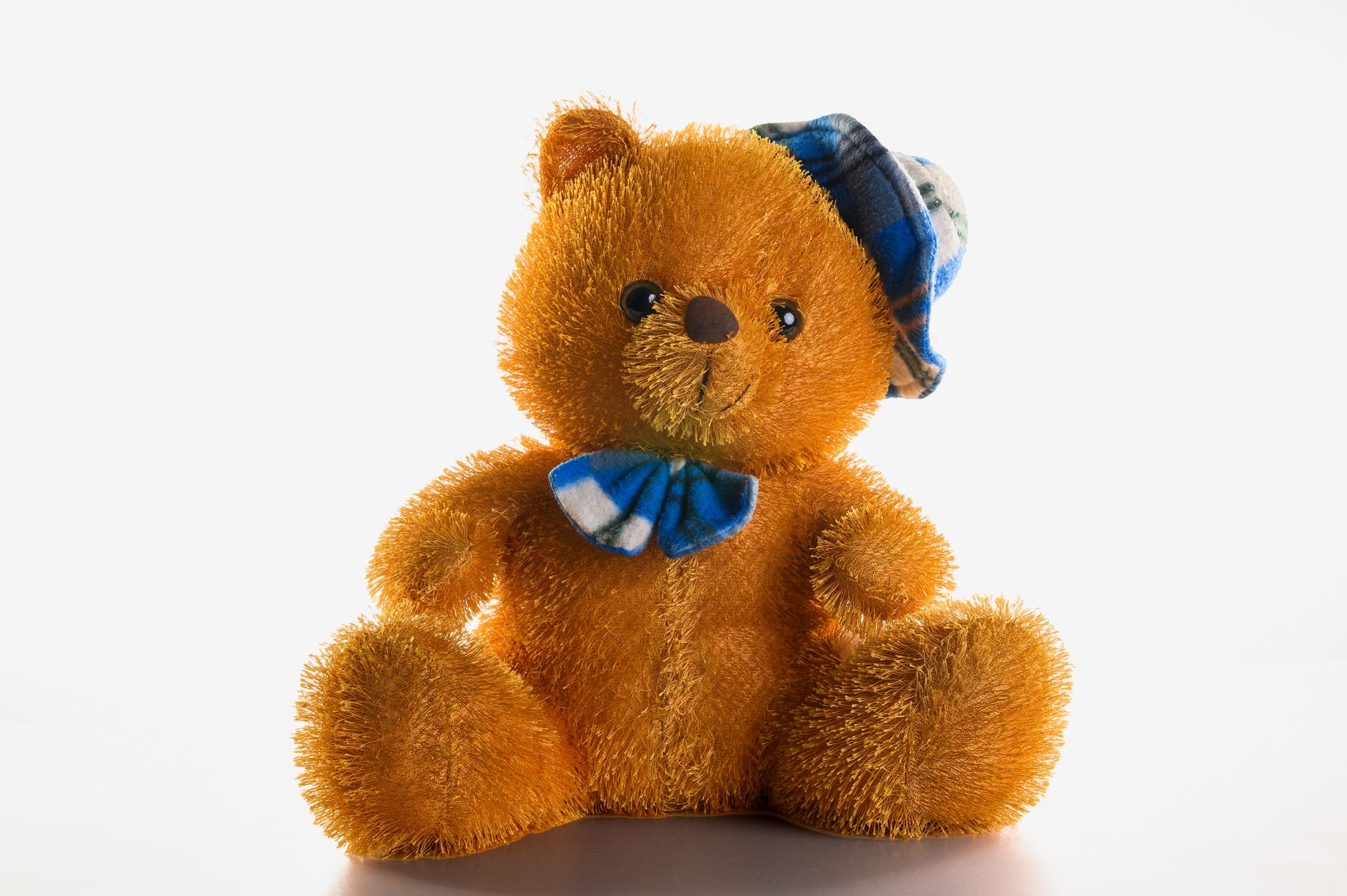 Adorable plush teddy bear with a blue bow tie and plaid hat, isolated on a white background.