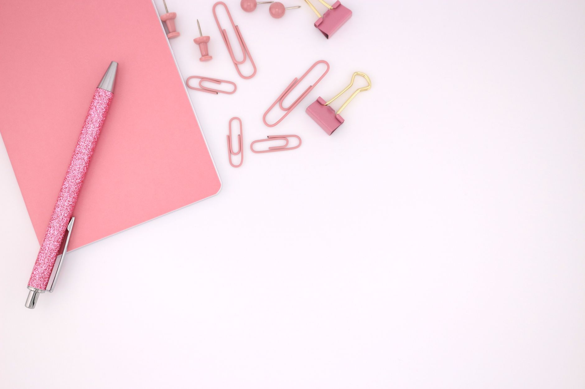 Aesthetic arrangement of pink office supplies with notebook on a white background.