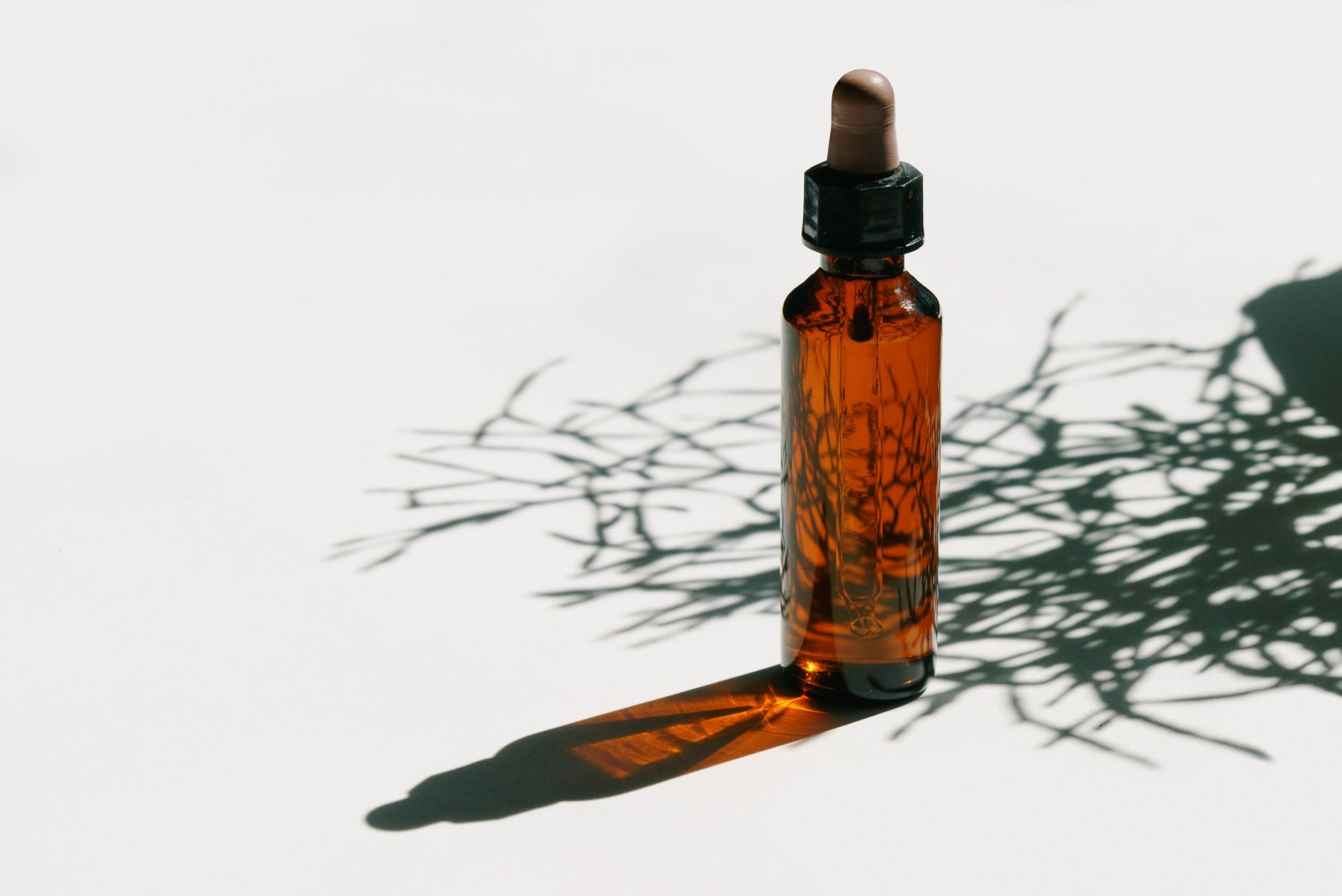 Brown glass dropper bottle casting shadows in a minimalist setting, ideal for beauty or health products.