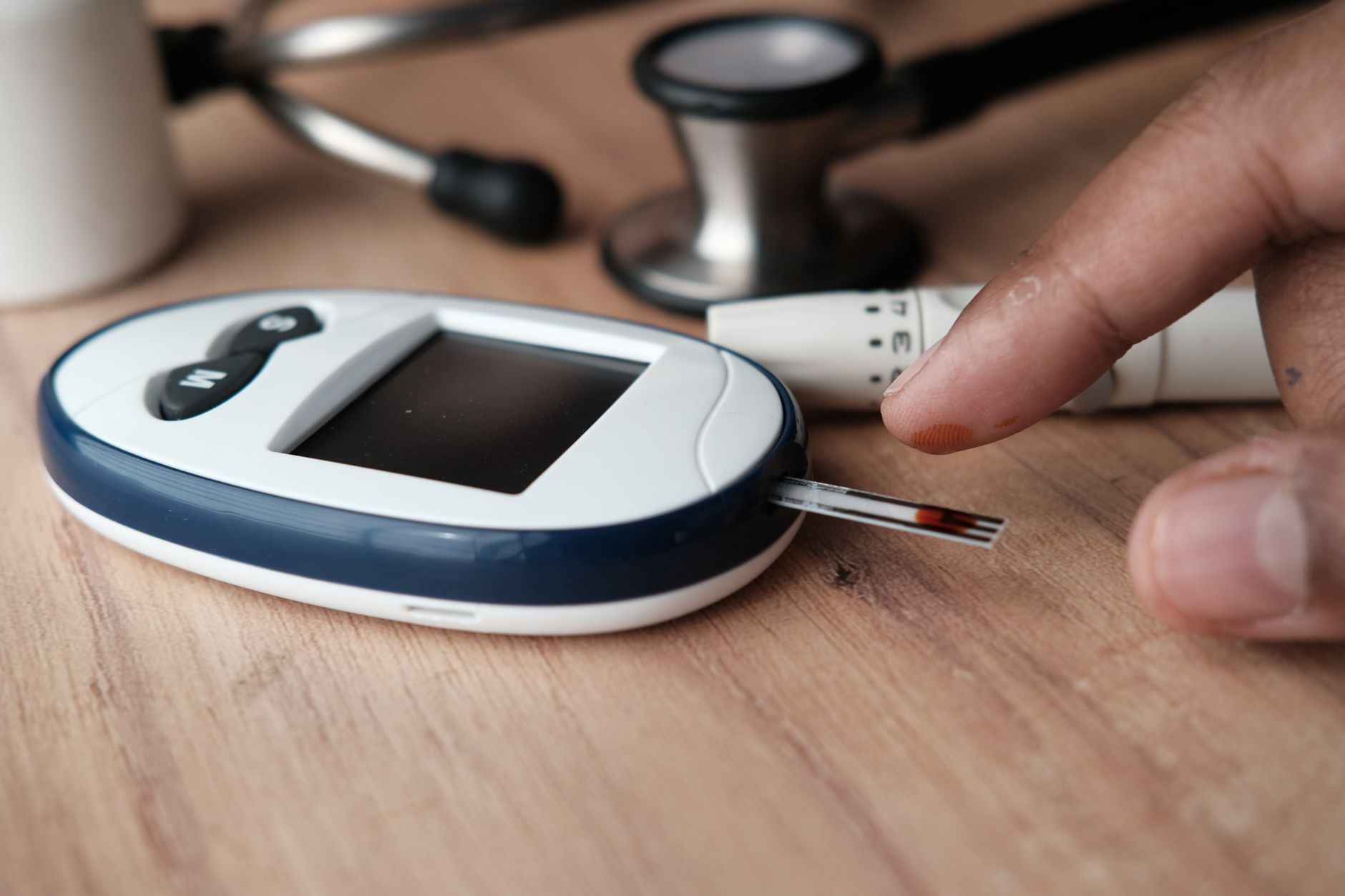 Close-up image of a glucometer checking blood sugar level with a finger pricking device nearby.