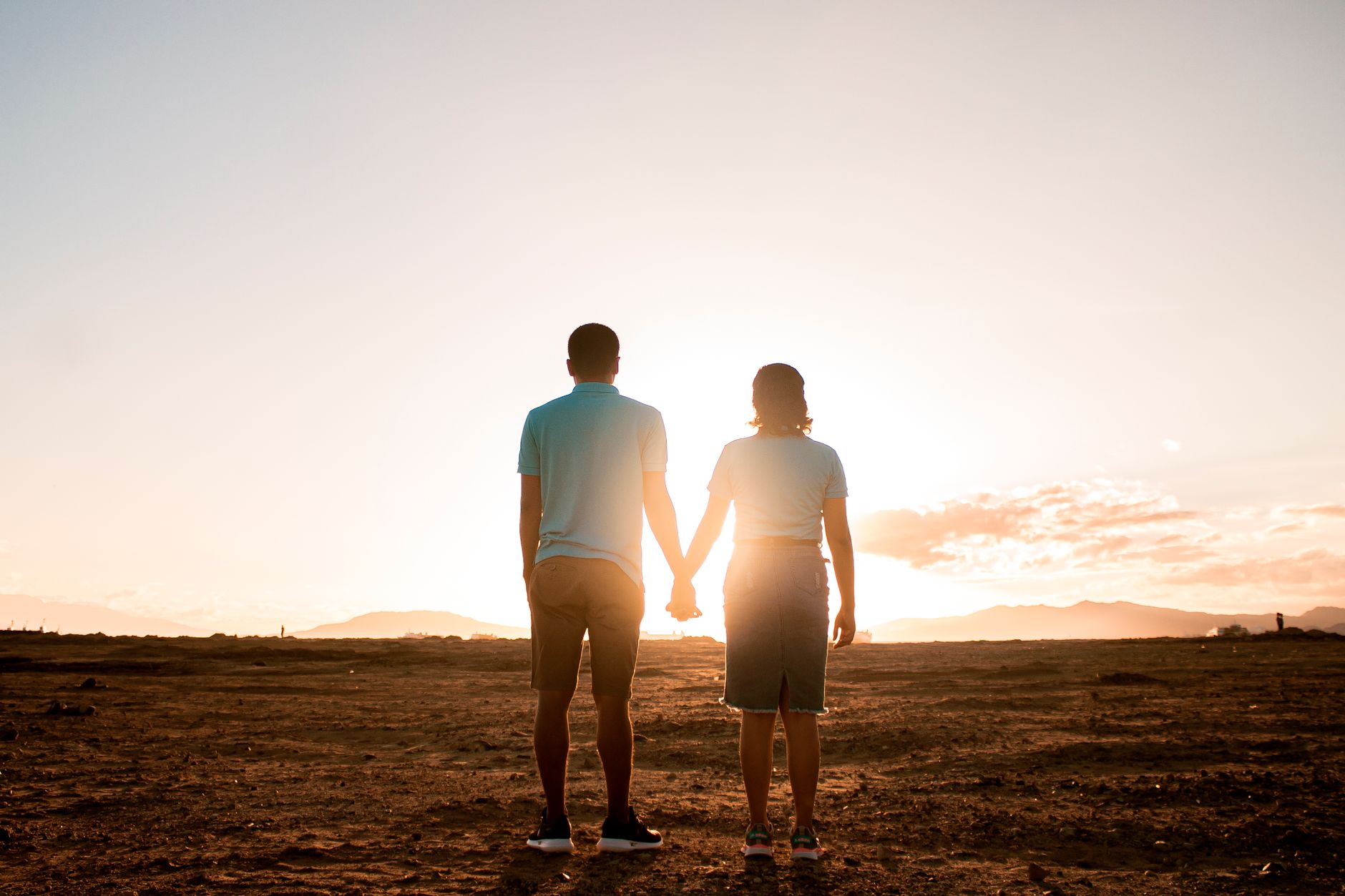 Couple holding hands at sunset in a serene rural landscape, expressing love and connection.